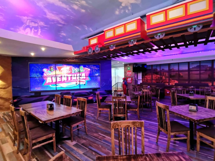Interior de Pizza Grizzly, Cayalá, con tren decorativo suspendido, cielo falso temático e iluminación de colores.